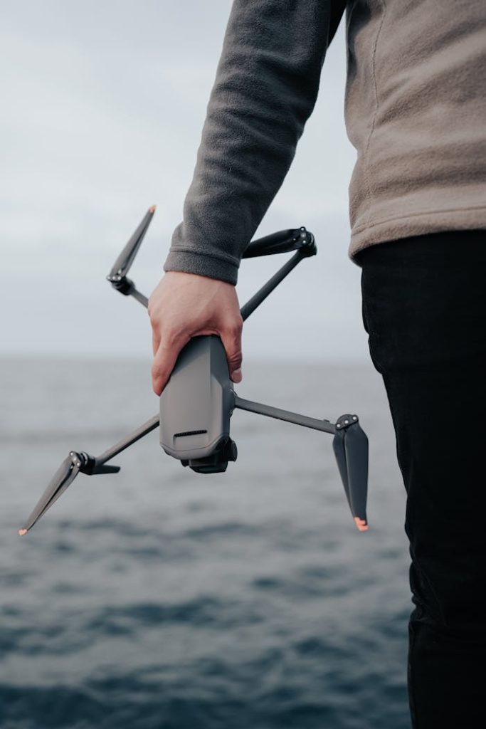 A close-up of a person holding a drone near the ocean, highlighting technology and exploration.