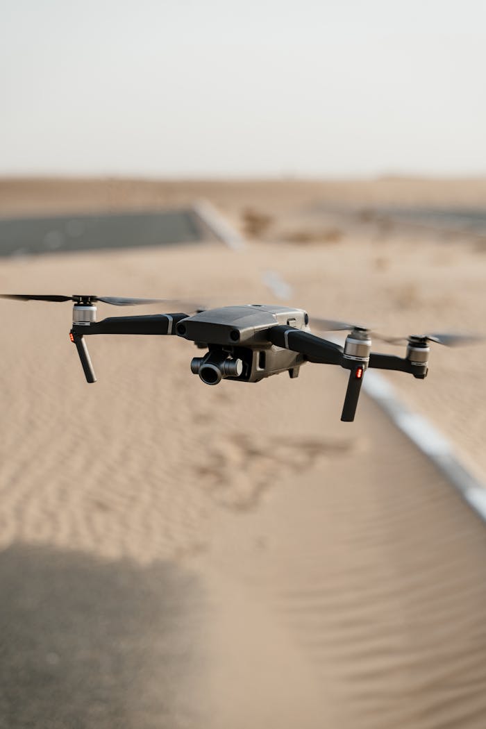 A black drone hovering over a sandy desert terrain, capturing scenic views.